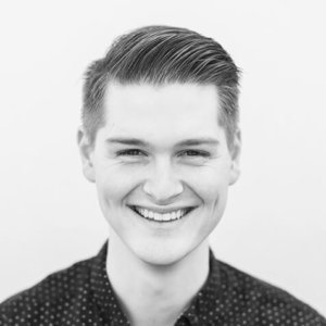 Professional headshot of smiling young man in polka dot shirt with grey background