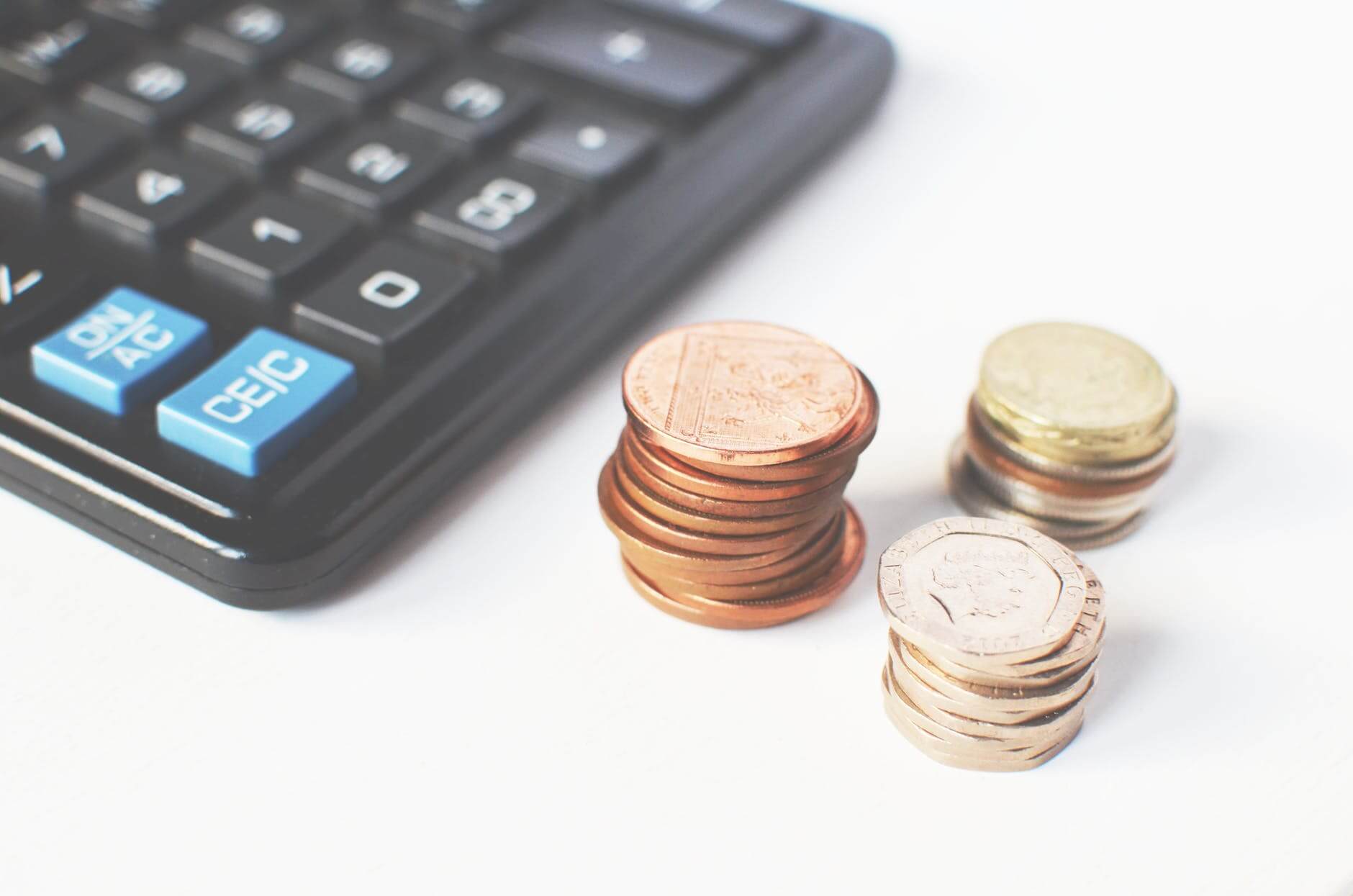 Financial planning scene with calculator and stacked coins - copper pennies, gold dollars, and silver coins on white surface