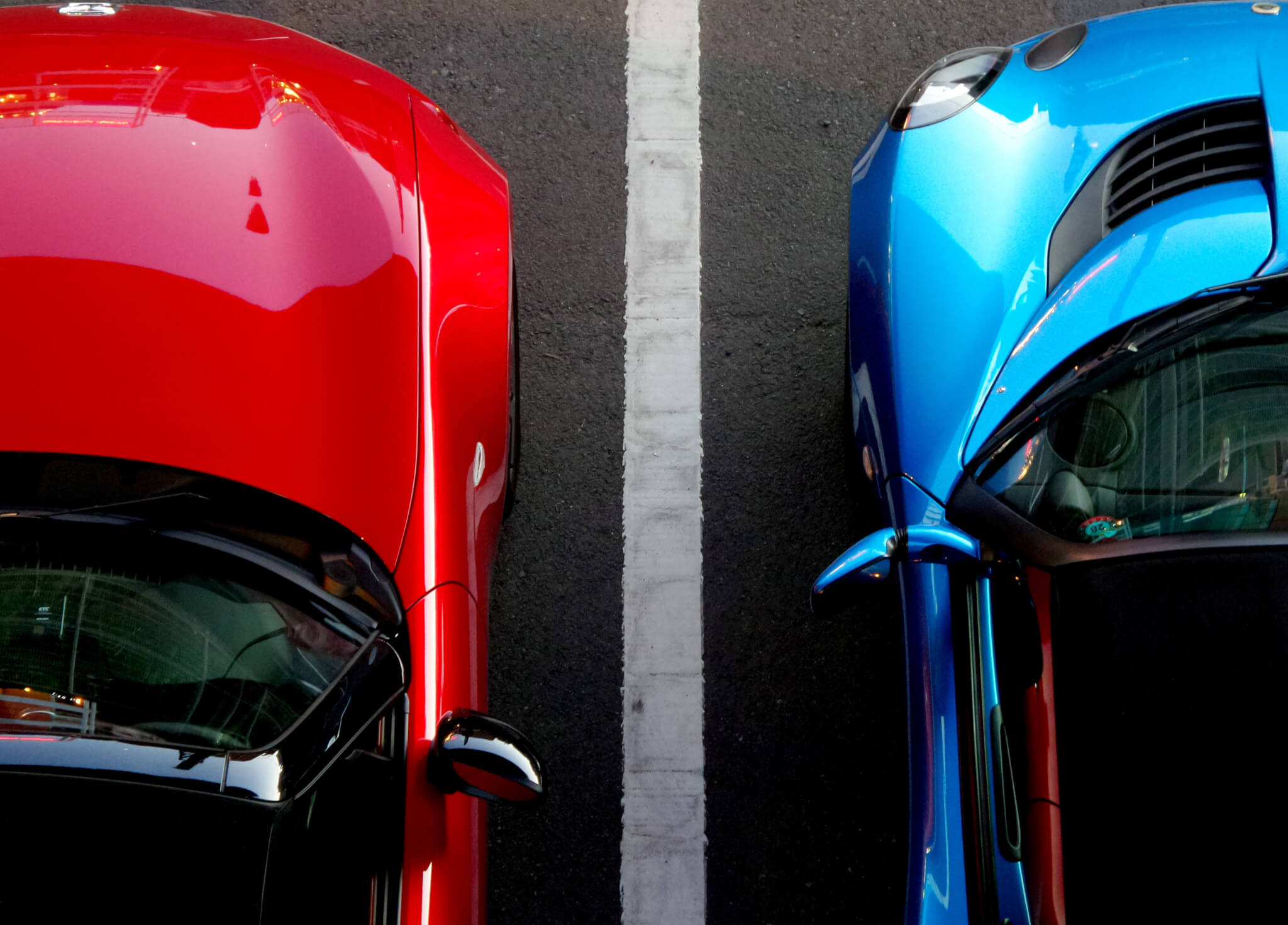 Overhead view of red and blue cars parked side by side with white parking line separator
